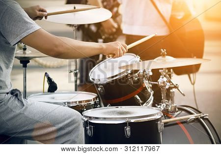 The Drummer In Gray Clothes Plays On A Black And Red Drum Set With Wooden Drumsticks. He Performs In
