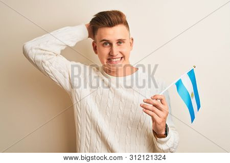 Young handsome man holding Argentinian Argentina flag over isolated white background stressed with hand on head, shocked with shame and surprise face, angry and frustrated. Fear and upset for mistake.