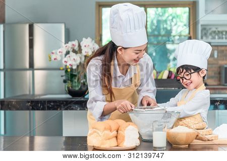Young Family Cooking Food In Kitchen. Happy Young Girl With Her Mother Mixing Batter In The Bowl.