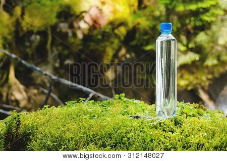 Plastic Bottle Blue Cap With Fresh Drinking Water On A Background Of Green Forest Stands On A Stone 