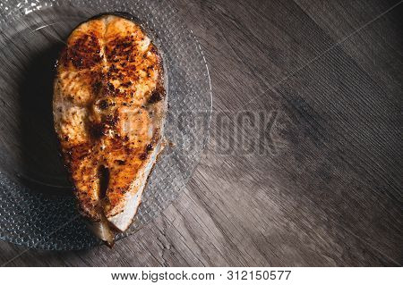 Close-up One Grilled Cum Salmon Keta Fish Steak On A Glass Transparent Plate On A Dark Wood Table Ba