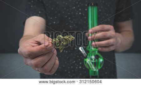The Young Person Hold In His Hand Medical Marijuana Buds And Bong. Smoking Medical Cannabis With Bon