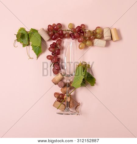 Alphabet. Letter T Made Of Wineglasses With Rose And White Wine, Grapes, Leaves And Corks Lying On P
