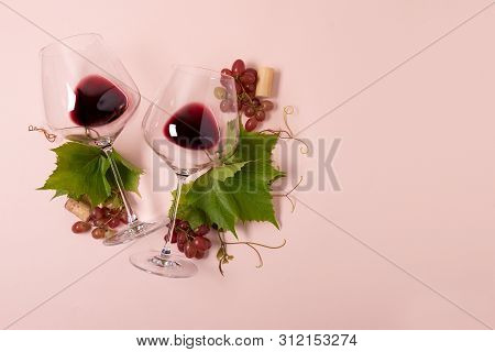 Wineglasses With Red Wine, Grape, Leaves And Cork Lying On Pink Background. Wine Degustation Concept