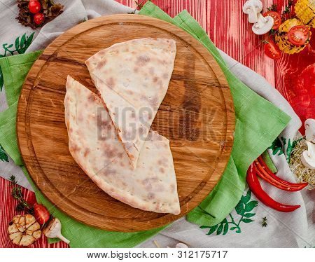 Half Of The Baked Calzone - Closed Type Of Pizza That Is Folded In Half, On A Round Wooden Board On 