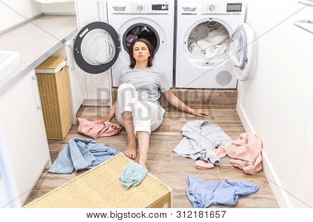 Sad Woman Sitting In Laudry Room With A Pile Of Dirty Clothes