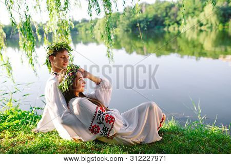 Midsummer. Young Loving Couple In Slavic Costumes On The Shore Of The Lake. Slavonic Holiday Of Ivan