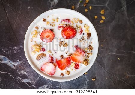 Muesli With Chocolate And Fresh Strawberries With Milk In A Plate On A Dark Gray Background. The Con