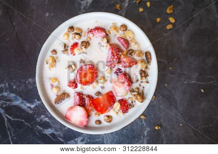 Muesli With Chocolate And Fresh Strawberries With Milk In A Plate On A Dark Gray Background. The Con