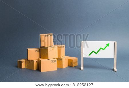 A Pile Of Cardboard Boxes And Stand With Green Up Arrow. Price Increase. The Growth Rate Of Producti