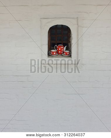 Tea Set Of Dotted Red And White Teapot And Cups On The Window Of Old White Brick House. Facade With 