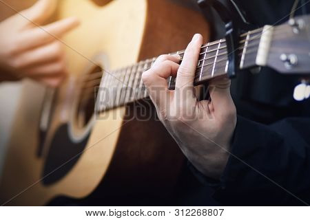 A Man In Black Clothes Playing On A Wooden Acoustic Six-string Guitar Beautiful Melody, Holding His 