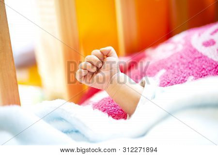 Hand Of An Energetic Newborn Baby With Light Blue And Pink Blanket And Baby Bed. Close Up.