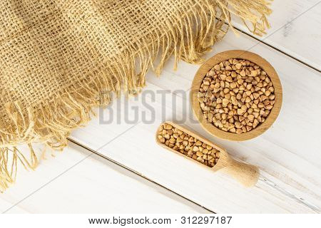 Lot Of Whole Raw Brown Buckwheat Grains In A Wooden Bowl And A Scoop With A Piece Of Jute Cloth Flat