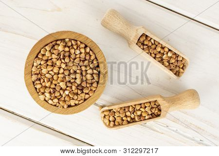 Lot Of Whole Raw Brown Buckwheat Grain In A Wooden Bowl With Wooden Scoop Flatlay On White Wood