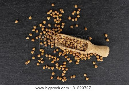 Lot Of Whole Raw Brown Buckwheat Grain With Wooden Scoop Flatlay On Grey Stone