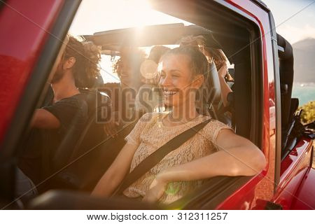 Happy millennial friends on a road trip vacation driving in an open car, close up, lens flare