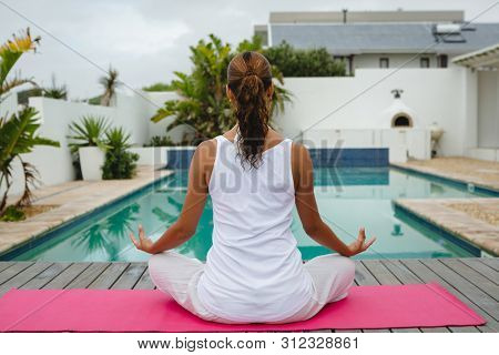 Rear view of fit mixed-race woman performing yoga near swimming pool in the backyard. Summer fun at home by the swimming pool