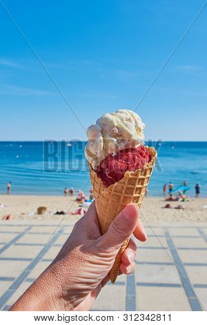 Hand Is Holding Ice Cream Cone In Front Of A Beach In Brittany, France