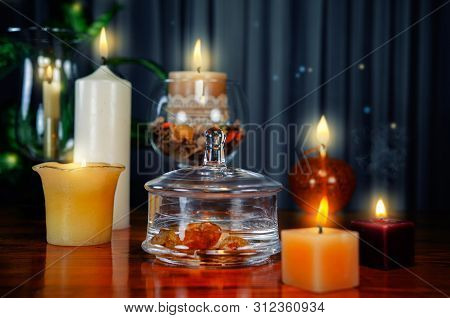 The purified water in the glass jar is charged with the energy of carnelian. The process of the making gem elixir is in progress, surrounded by lit candles on a wooden table.