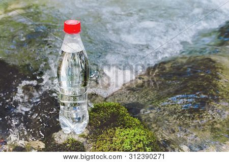 A Plastic Bottle With A Red Cap With Fresh Drinking Water Against A Background Of Green Forest And A