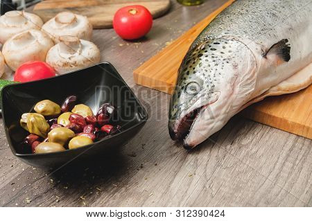 Close-up Keta Fish, Whole On The Cutting Board Of The Kitchen Table Next To Olives Tomatoes And Mush