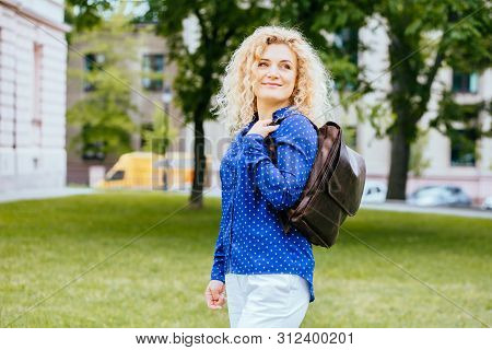 Adorable Blond Curly Haired Woman In Blue Shirt And Brown Leather Bacpack, Outdoor Summer Portrait. 