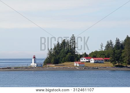 Inside Passage, Canada - August 5, 2006 - Lighthouse And Red-roofed Buildings With Evergreen Forest 