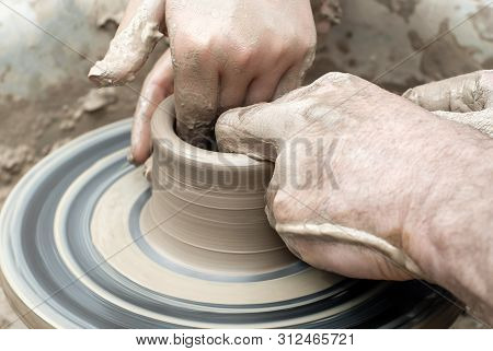 Two Pairs Of Hands Mold Something From Clay On A Potter's Wheel