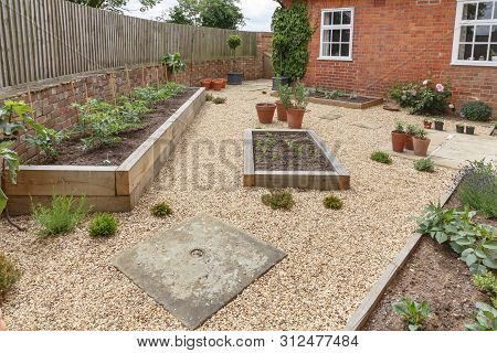 Oak Sleeper Raised Beds In A Courtyard Garden Design With Hard Landscpaing, Gravel And Terracotta Po