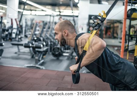 Instructor At The Gym Doing Excersise. Fitness Man Workout On The Rings.