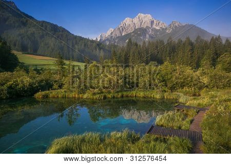 Lake Zelenci, Source Of The Sava Dolinka River With The Observation Trail Footbridge And Ponce Mount