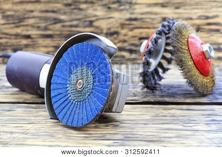 Angle Grinder With Grinding Disc Brushes And Abrasive Wire Brushes Lies On The Background Of A Woode