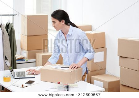 Busy manager of oline shop with packed box looking through order information