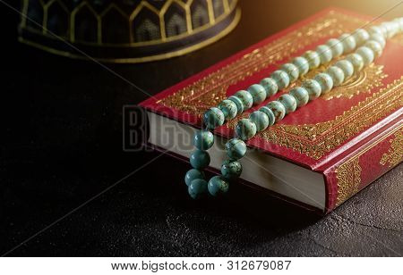 The Holy Quran With Rosary Beads And Kopiah Hat For Muslims On Black Table