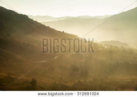 Stunning Autumn Fall Landscape Sunrise In The Lake District With Sun Beams Streaming Through The Mis