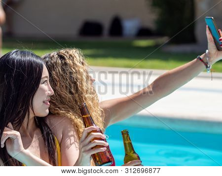 Caucasian Girl And Oriental Girl Play And Laugh In The Pool, Drinking Beer