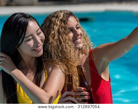 Caucasian Girl And Oriental Girl Play And Laugh In The Pool, Drinking Beer