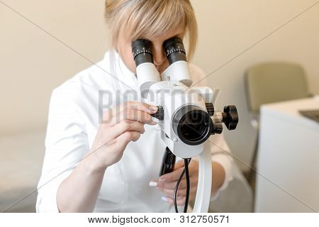 Young Female Professional Gynecologist In The Working Process, Looks Into The Colposcope.