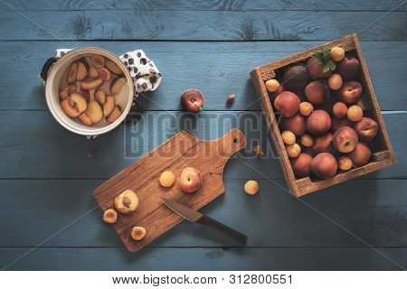 Box With Fresh Peaches And Apricots, Slicing Fruits On Cutting Board And Pot With Fruit Pieces For M