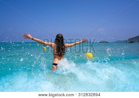 Ibiza beach girl splashing water open arms in Balearic islands