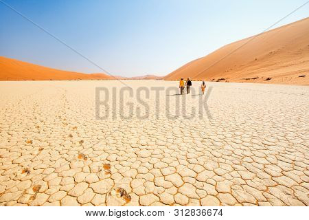 Back view of family father and two kids walking at white clay pan surrounded by red dunes in Deadvlei in Namibia