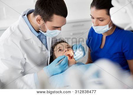 medicine, dentistry and healthcare concept - dentist with mouth mirror and probe checking for kid patient teeth at dental clinic