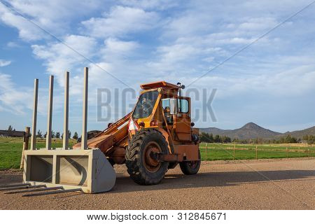 Side Angle Of Orange Tractor With A Plow In A Field With Blue Sky In The Background