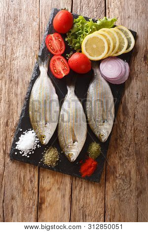 Preparation For Cooking Sarpa Salpa Fish With Lemon, Vegetables And Spices Close-up On A Slate Board