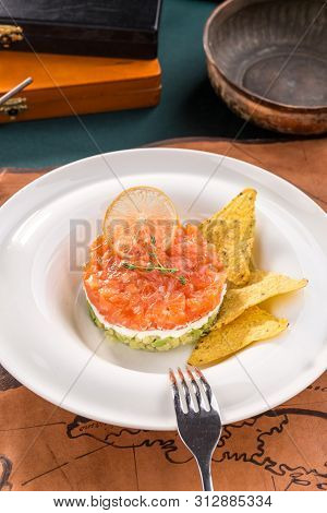 Tartar With Salmon, Avocado, Cream Cheese And Nachos On White Plate On Old Map Background Side View