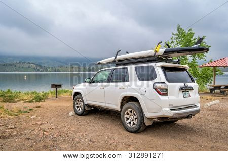 Fort Collins, CO, USA - July 22, 2019: Toyota 4Runner SUV with a performace stand up paddleboard on roof racks at a picnic and swimming area on shore of Horsetooh Reservoir on a foggy summer morning.