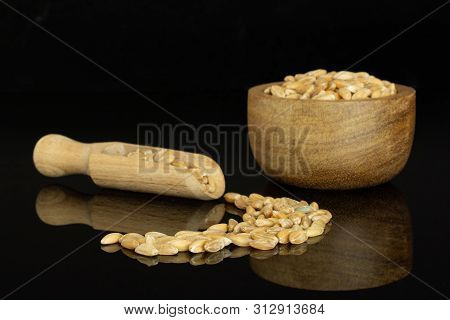 Lot Of Whole Fresh Beige Dinkel Wheat Grain With Wooden Scoop In A Wooden Bowl Isolated On Black Gla