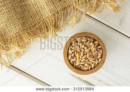 Lot Of Whole Fresh Beige Dinkel Wheat Grain In A Wooden Bowl And Jute Cloth Flatlay On White Wood