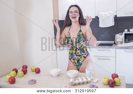 Happy Woman In Fashionable Swimsuit With Green Leaves Posing In White Kitchen
